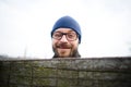 Funny young man with glasses and a beard looks out from behind the fence. He Royalty Free Stock Photo