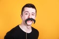 Funny young man holding a fake moustache in a stick in front of his face on yellow background Royalty Free Stock Photo