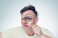 Funny young man looking through magnifying glass, on light background