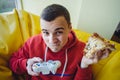 Funny young man playing video game on the joystick and eat delicious pizza.