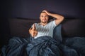 Funny young man sitting on bed and smiling. He shows big thumb up on one hand and hold another one on head. Guy is Royalty Free Stock Photo