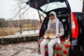 Happy young man in white sweater holding Christmas gift box and bunny in car trunk. Royalty Free Stock Photo