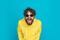 Funny young man in yellow hoodie opening mouth and laughing