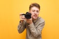 Funny young photographer with mustache and glasses isolated with camera in hand on yellow background, looking into camera with Royalty Free Stock Photo