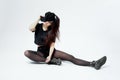 Funny young stylish girl dressed in a black top, shorts, tights and cap sits on the floor on the white background in the Royalty Free Stock Photo