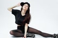 Funny young stylish girl dressed in a black top, shorts, tights and cap sits on the floor on the white background in the Royalty Free Stock Photo