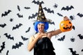 Funny young woman in a blue wig and witch`s hat holds Halloween pumpkin on a white background with black bats and Royalty Free Stock Photo