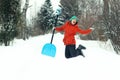 Funny young woman jump with snow shovel on rural road. Winter seasonal concept