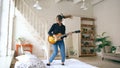 Funny young woman in headphones jumping on bed with electric guitar in bedroom at home indoors Royalty Free Stock Photo