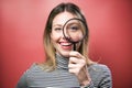 Funny young woman looking through magnifying glass at the camera over pink background Royalty Free Stock Photo