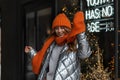 Funny young woman with red hair in a knitted fashion hat with a vintage orange scarf in a youth silver jacket posing near a glass Royalty Free Stock Photo