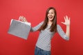 Funny young woman showing palm, waving hand, holding packages bags with purchases after shopping isolated on bright red Royalty Free Stock Photo