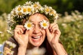 A funny young woman in a wreath of daisies is laughing and holding daisies in front of her eyes. On a large field of daisies Royalty Free Stock Photo
