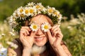 A funny young woman in a wreath of daisies is laughing and holding daisies in front of her eyes. On a large field of daisies Royalty Free Stock Photo