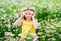 A funny young girl in a wreath of daisies laughs and holds flowers in front of her eyes. The screen is covered with flowers. In a Royalty Free Stock Photo