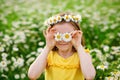 A funny young girl in a wreath of daisies laughs and holds flowers in front of her eyes. The screen is covered with flowers. In a Royalty Free Stock Photo