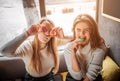 Funny young women cover eyes with macarons. They pose on camera. Brunette bites piece of macarone. They have fun.
