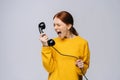 Furious angry young woman in stylish yellow sweater talking on retro phone and screaming in handset. Royalty Free Stock Photo