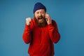 Furious man shouting and clenching his fist while talking on mobile phone isolated over blue wall Royalty Free Stock Photo