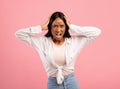 Furious black woman screaming and holding her head on pink studio background