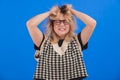 Furious female university student disheveling her blonde hair over blue background. Copy space studio shot. Royalty Free Stock Photo