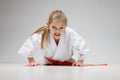 Furious little girl doing push-ups in kimono, karate training on a white background