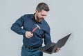 Furious man break laptop hitting notebook with hammer grey background, computer rage