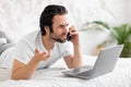 Furious man making phone call and using laptop in bed Royalty Free Stock Photo