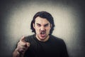 Furious young man pointing forefinger to camera blaming someone as guilty, or scolding  on grey wall background. Angry guy Royalty Free Stock Photo