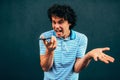 Furious young man talking on a mobile phone with his girlfriend. Mad male student with curly hair making a call on his smartphone Royalty Free Stock Photo