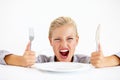 This is ridiculous Im starving. Furious young woman sitting in front of an empty plate while holding her knife and fork. Royalty Free Stock Photo