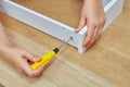 Furniture assembler tightens the into a wooden chipboard drawer using a screwdriver, ready-to-assemble furniture