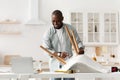 Furniture assembly. Happy african american man screwing detail to chair, looking at laptop at manual in blog