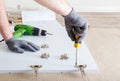 Furniture assembly using screwdriver. Male hands in gray gloves master collects furniture using screwdriver tools, instrument at Royalty Free Stock Photo