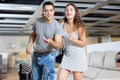 Husband and wife are standing in furniture store among huge assortment of sofas