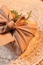 Furoshiki technique. Gift packed in beige fabric with blank card on plate, closeup