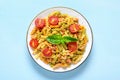 Fusilli - classic italian pasta from durum wheat with chicken meat, tomatoes cherry, basil in tomato sauce in white bowl on blue Royalty Free Stock Photo