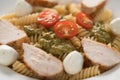 Fussili pasta with chicken fillet, tomatoes, mozzarella and pesto sauce in white bowl closeup