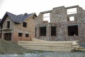 Future cottage under construction and pile of gravel and stack of boards in front of not finished new big brick house with brown s Royalty Free Stock Photo