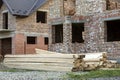 Future cottage under construction and pile of gravel and stack of boards in front of not finished new big brick house with brown Royalty Free Stock Photo