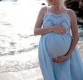 Future mother belly, pregnant woman posing near ocean in white lace dress Royalty Free Stock Photo