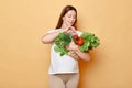 Future mother buying organic food, pregnant woman holding fresh vegetables posing isolated over beige background, prefers useful Royalty Free Stock Photo