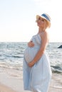 Future mother posing near ocean in blue provence style dress and hat