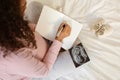 Future mother writing in journal beside baby sonogram and tiny shoes