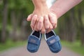 Future parents holding hands and a pair of little shoes over blur park background. Concept of Parents-To-Be Royalty Free Stock Photo