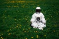 Futuristic astronaut in a helmet sits on a green lawn among flowersin a meditative position