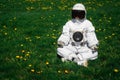 Futuristic astronaut in a helmet sits on a green lawn among flowersin a meditative position