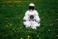 Futuristic astronaut in a helmet sits on a green lawn among flowersin a meditative position Royalty Free Stock Photo