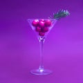 Futuristic Christmas party concept. Martini glass full of small red Christmas ornament with green little spruce against violent