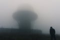 A futuristic concept of a hooded figure standing by a radar base on moorland. On a spooky, foggy day